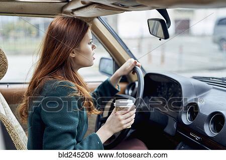 Stock Photo - Angry Caucasian woman driving car and drinking coffee. Fotosearch