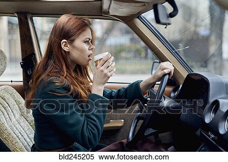 Stock Photography - Angry Caucasian woman driving car and drinking coffee. Fotosearch