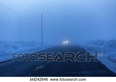 Stock Photograph - Approaching headlights from car driving in winter. Fotosearch