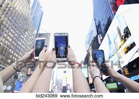 Stock Photo - Arms of Caucasian women photographing skyscrapers with cell phones. Fotosearch