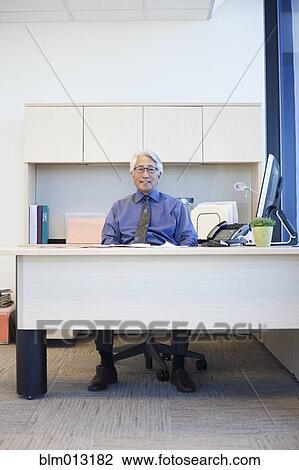 Stock Image - Asian businessman sitting at desk. Fotosearch