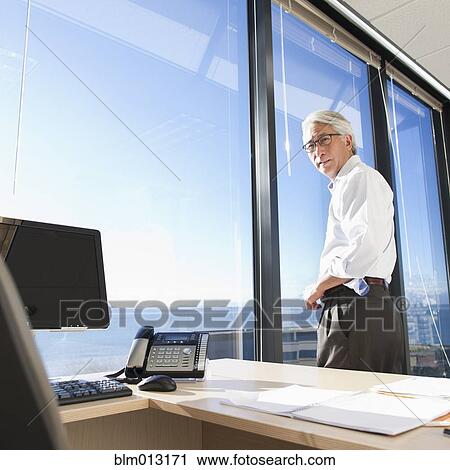 Stock Image - Asian businessman standing at office window. Fotosearch