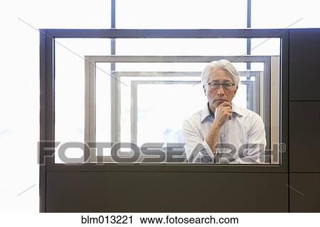 Stock Image - Asian businessman standing in office cubicle. Fotosearch