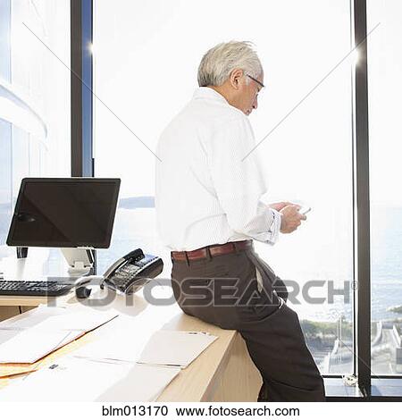 Stock Image - Asian businessman using cell phone in office. Fotosearch
