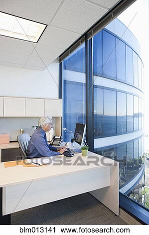 Stock Image - Asian businessman working at desk. Fotosearch