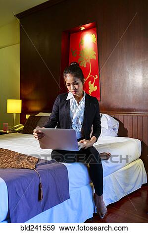 Stock Photo - Asian businesswoman sitting on hotel bed using laptop. Fotosearch