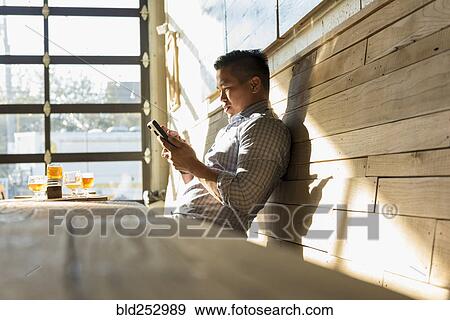 Stock Photo - Asian man texting on cell phone in brew pub. Fotosearch