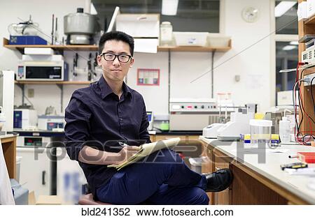 Stock Image - Asian man writing on notepad in electronics workshop. Fotosearch