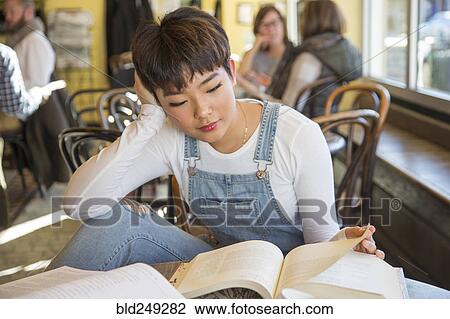 Stock Image - Asian teenage girl reading book in coffee shop. Fotosearch