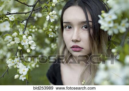 Stock Photo - Asian teenage girl standing in branches with flowers. Fotosearch