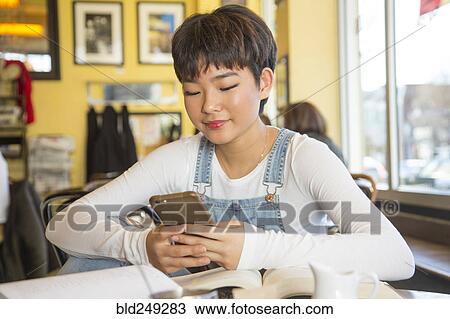 Asian teenage girl texting on cell phone in coffee shop View Large Photo Image Stock Image - Asian teenage girl texting on cell phone in coffee shop. Fotosearch
