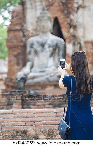 Stock Photo - Asian woman photographing Buddha statue with cell phone. Fotosearch