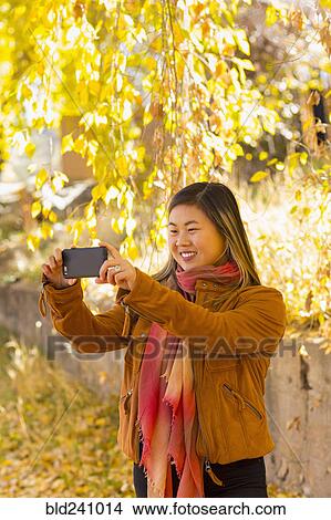 Picture - Asian woman posing for cell phone selfie in autumn. Fotosearch