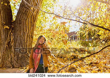 Picture - Asian woman talking on cell phone in autumn. Fotosearch