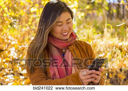 Asian woman texting on cell phone in autumn View Large Photo Image Stock Image - Asian woman texting on cell phone in autumn. Fotosearch