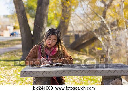 Asian woman writing in journal on table in autumn View Large Photo Image Stock Photo - Asian woman writing in journal on table in autumn. Fotosearch