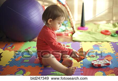 Stock Photo - Baby boy sitting on playroom floor holding book. Fotosearch