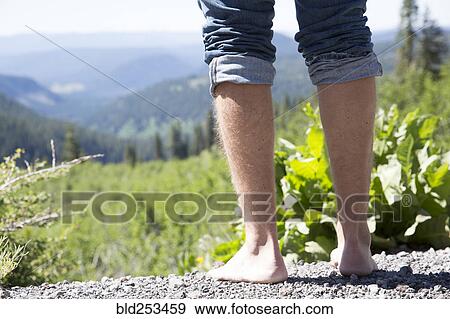 Stock Photo - Barefoot Caucasian man standing near mountain landscape. Fotosearch