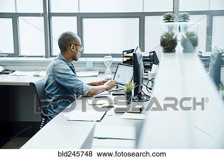 Stock Photo - Black businessman using laptop in office. Fotosearch