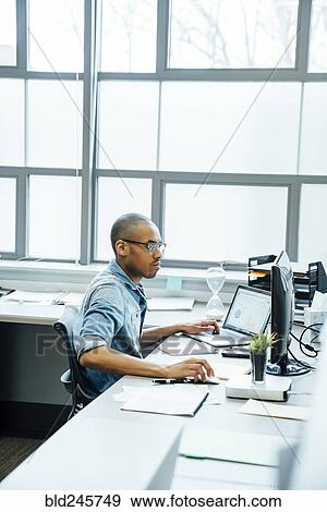 Stock Photo - Black businessman using laptop in office. Fotosearch