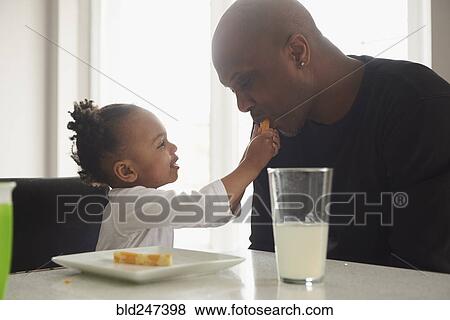 Stock Photo - Black daughter feeding food to father. Fotosearch