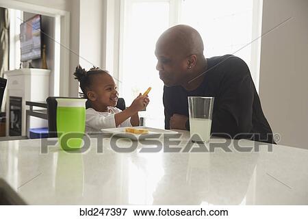 Stock Photo - Black daughter offering food to father. Fotosearch