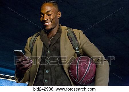 Black man holding basketball texting on cell phone View Large Photo Image Stock Photograph - Black man holding basketball texting on cell phone. Fotosearch