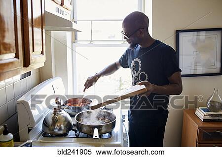 Stock Photography - Black man holding cutting board cooking on stove. Fotosearch