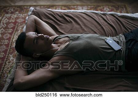 Black man laying on bed listening to music on cell phone View Large Photo Image Stock Photograph - Black man laying on bed listening to music on cell phone. Fotosearch