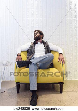 Stock Photograph - Black man sitting in yellow chair. Fotosearch