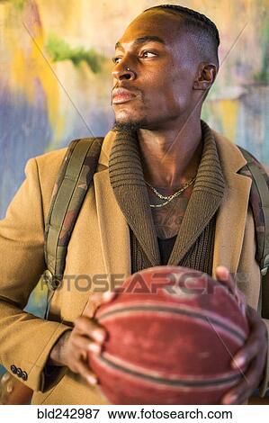 Stock Photo - Black man wearing backpack holding basketball. Fotosearch