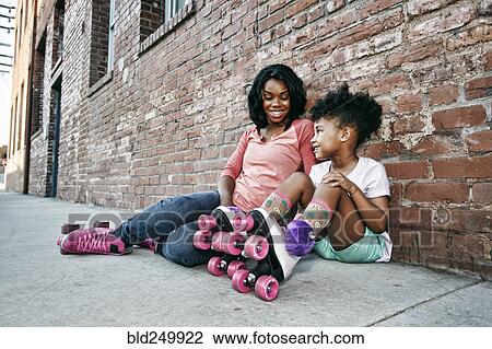 Black mother and daughter wearing roller skates sitting on sidewalk View Large Photo Image Stock Image - Black mother and daughter wearing roller skates sitting on sidewalk. Fotosearch