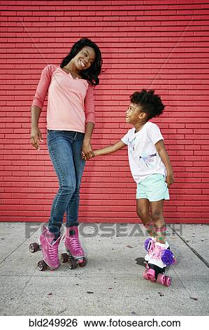 Stock Photograph - Black mother and daughter wearing roller skates holding hands. Fotosearch