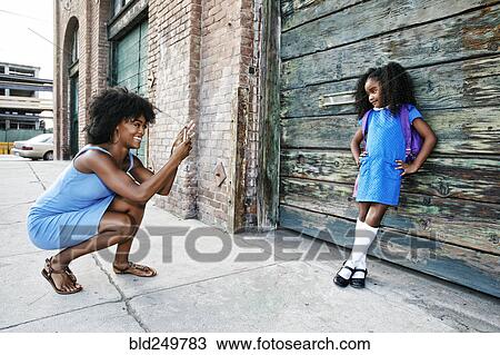 Black mother photographing daughter on sidewalk with cell phone View Large Photo Image Stock Image - Black mother photographing daughter on sidewalk with cell phone. Fotosearch