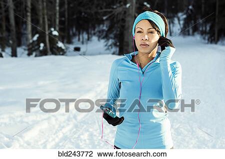 Stock Image - Black runner listening to cell phone with earbuds in winter. Fotosearch