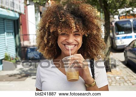 Stock Photo - Black woman drinking with straw on city sidewalk. Fotosearch