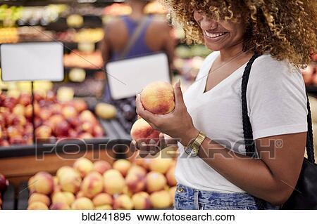Stock Photography - Black woman examining peaches in grocery store. Fotosearch