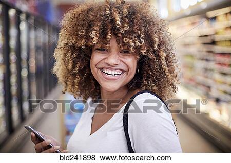 Black woman holding cell phone smiling in grocery store View Large Photo Image Stock Photo - Black woman holding cell phone smiling in grocery store. Fotosearch