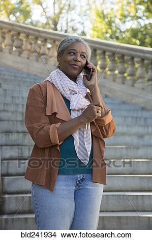Picture - Black woman on stone staircase talking on cell phone. Fotosearch