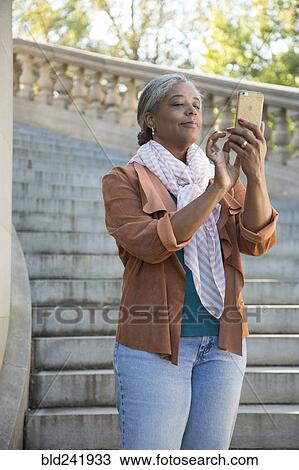 Stock Image - Black woman on stone staircase texting on cell phone. Fotosearch