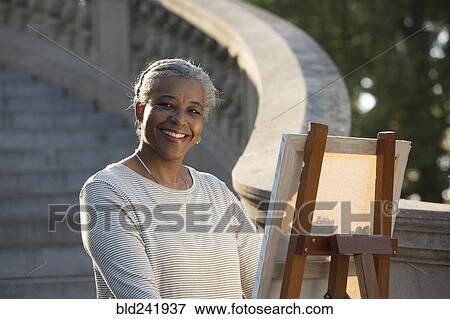 Stock Photo - Black woman painting on canvas near stone staircase. Fotosearch