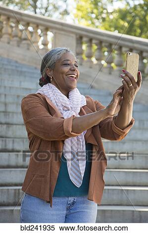 Stock Photography - Black woman posing for cell phone selfie on stone staircase. Fotosearch