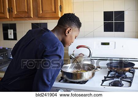 Picture - Black woman smelling food cooking in pan on stove. Fotosearch