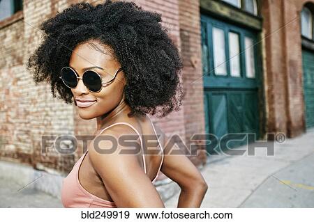 Stock Photo - Black woman smiling near corner of brick building. Fotosearch