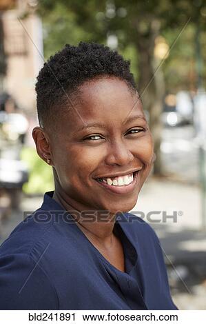 Stock Image - Black woman smiling on city sidewalk. Fotosearch