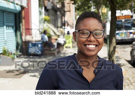 Stock Photo - Black woman wearing eyeglasses smiling on city sidewalk. Fotosearch