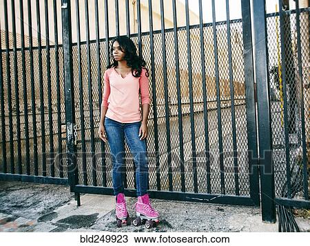 Stock Image - Black woman wearing roller skates near metal gate. Fotosearch