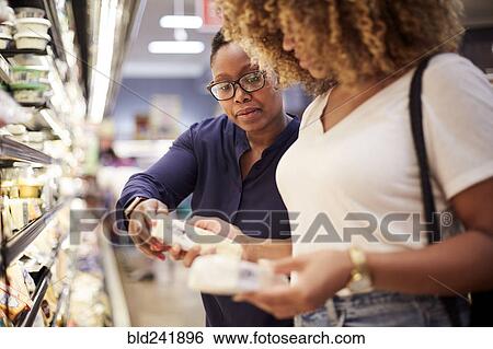 Stock Photograph - Black women examining cheese in grocery store. Fotosearch