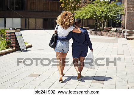 Stock Image - Black women walking and hugging in city. Fotosearch