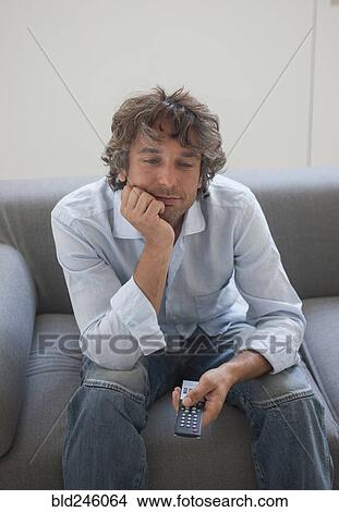 Bored Caucasian man sitting on sofa watching television View Large Photo Image Picture - Bored Caucasian man sitting on sofa watching television. Fotosearch